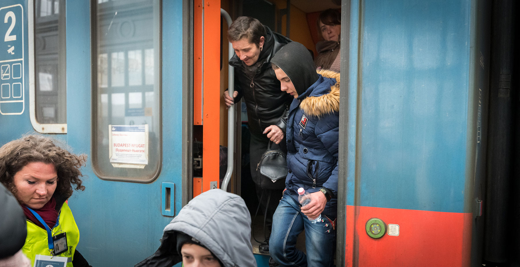 Families disembark a train at Nyugati station in Budapest, greeted by an aid worker supporting newly arrived families from Ukraine. The station has become a central entry point for refugees.  